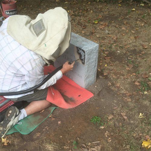 A CJ Stones craftsman in a blast hood cutting an inscription into a headstone at the cemetery
