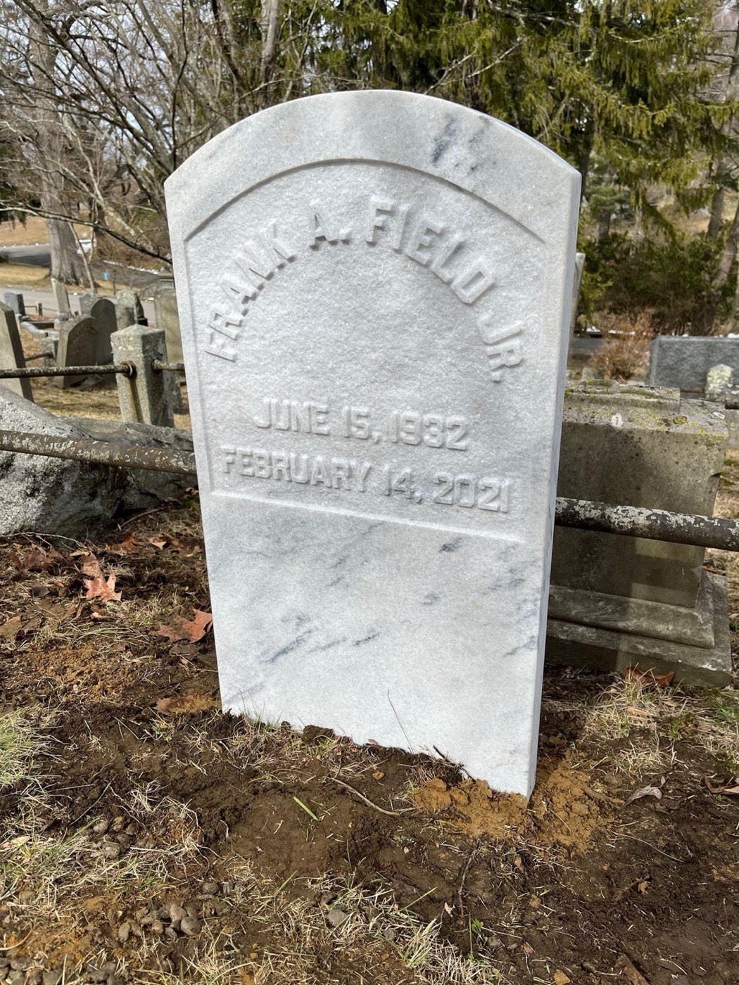 White marble headstone with arched cut lettering, newly set in a historic cemetery
