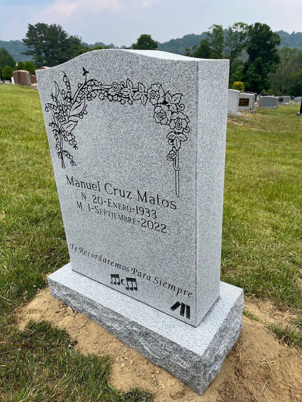 Light grey granite upright with a Spanish inscription and a carved lily and rose border