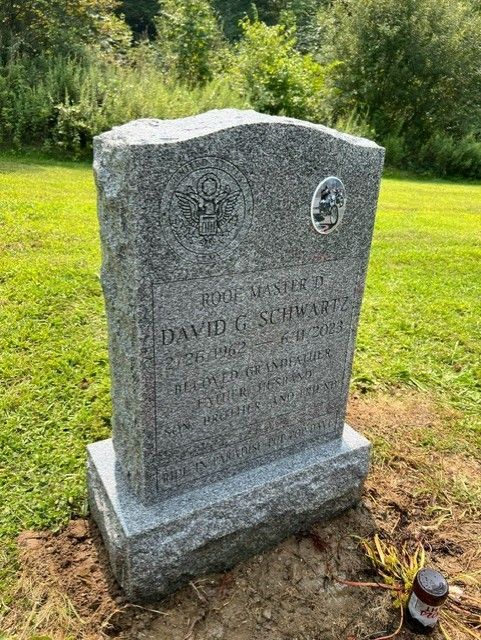 Grey granite upright with a United States military emblem and a porcelain portrait, standing in a cemetery