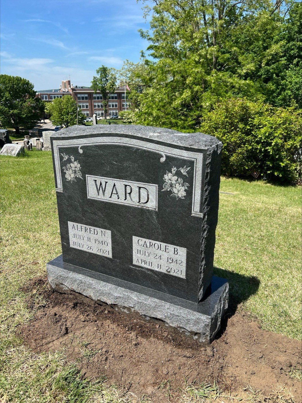 Dark grey granite upright monument with a polished panel, carved hummingbirds and lilies