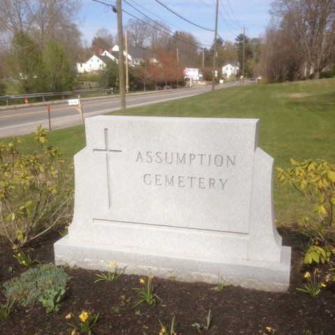 A cleaned and recut granite cemetery entrance sign reading Assumption Cemetery