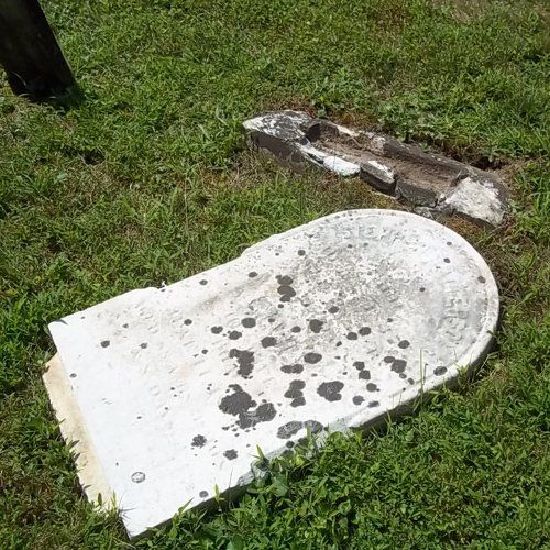A marble headstone lying flat on the grass, broken from its base and spotted with lichen