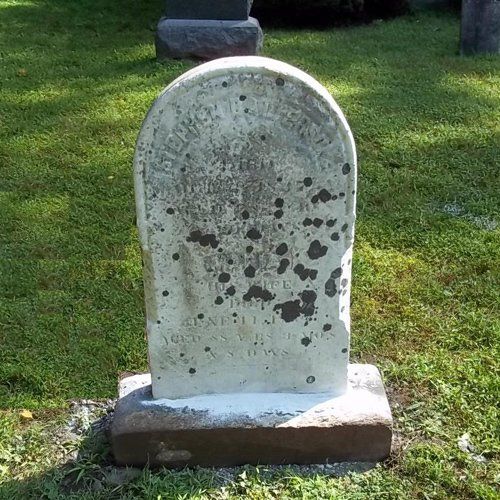 A marble headstone standing upright, still bearing dark lichen spotting