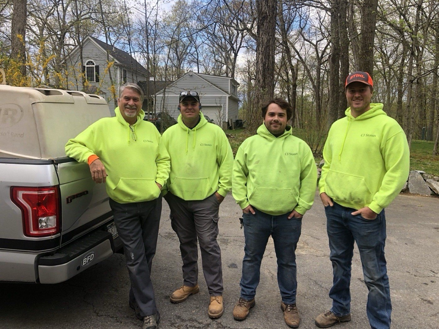 Four members of the CJ Stones crew in branded work clothing, standing beside the company truck