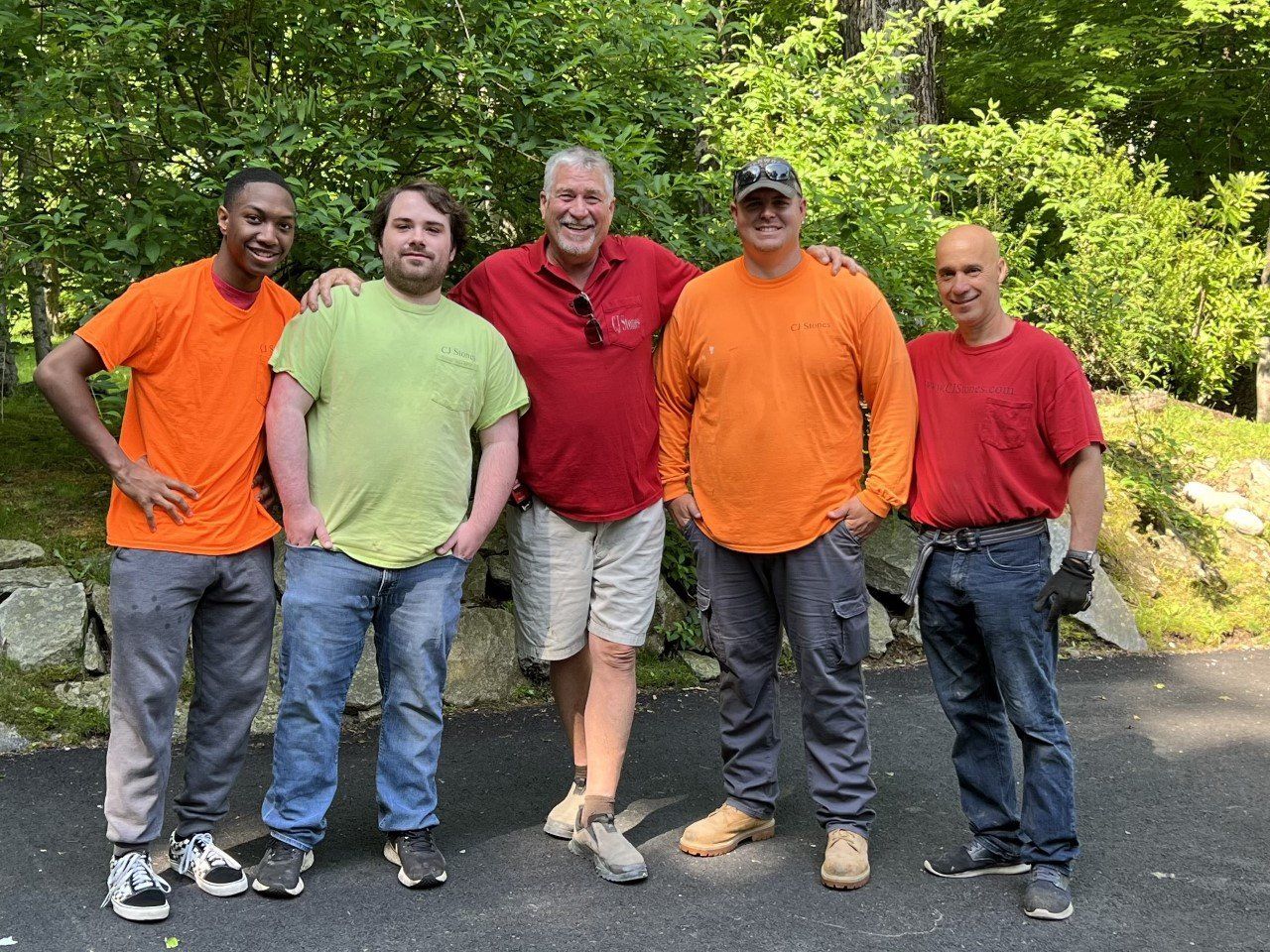 Five members of the CJ Stones crew in branded work shirts on a wooded drive